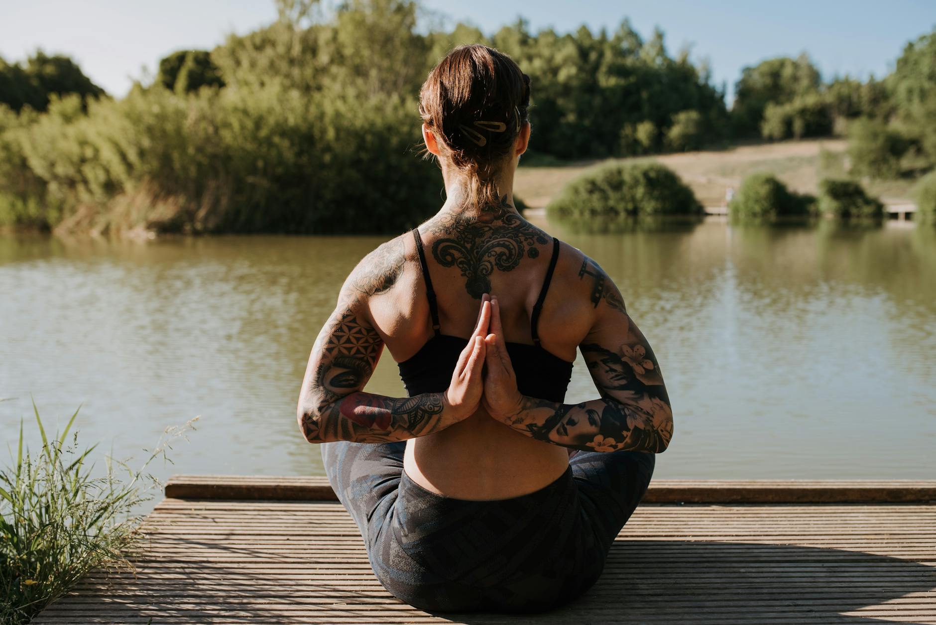Woman in a calm yoga pose on a wooden pier by the lake, surrounded by nature